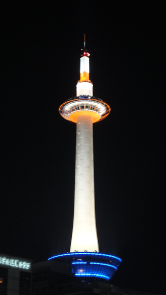 kyoto tower lit mostly white at night with orange near the top and blue at the base